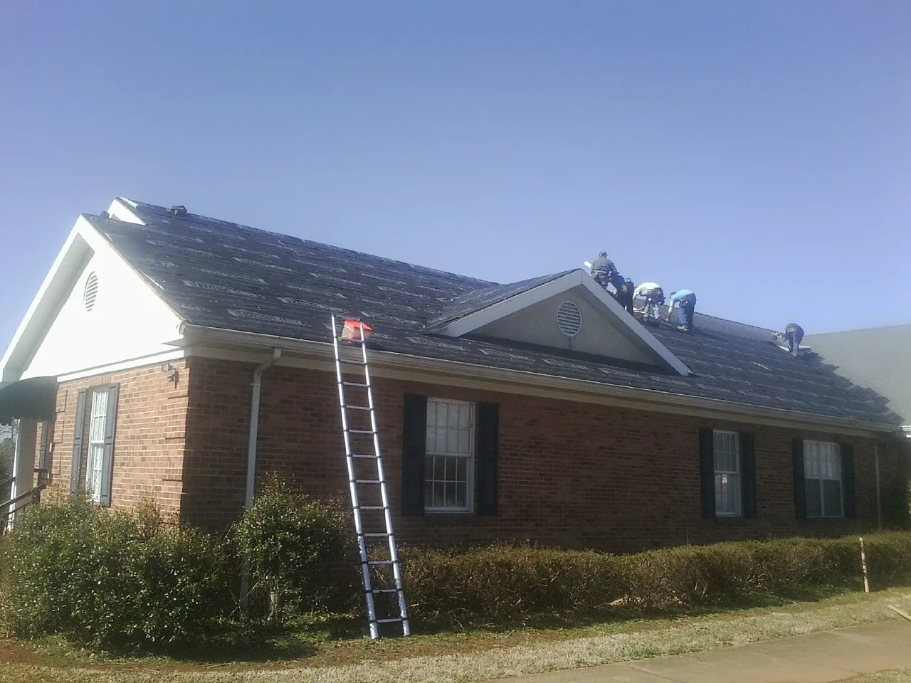 Crew tearing shingles off a brick ranch roof with a ladder set — Emergency Roof Repair work by our crew in Morgantown