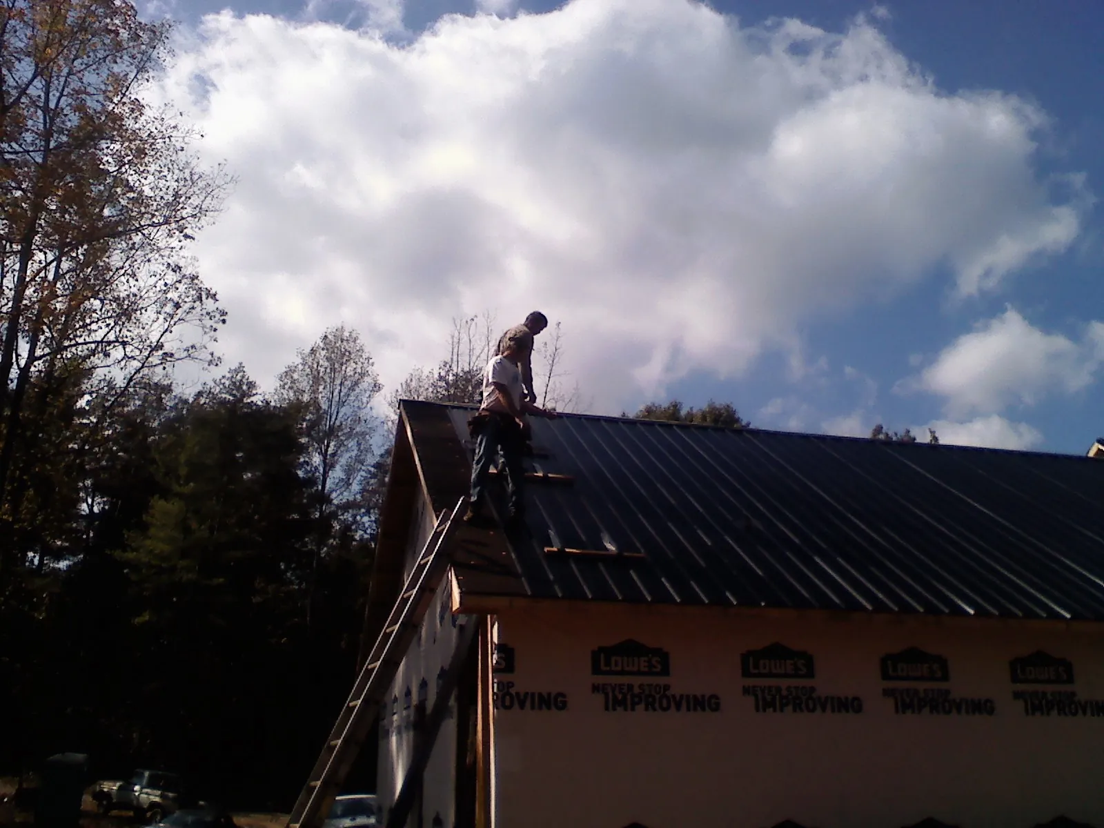 Roofer fastening dark metal panels high against a cloudy sky, from a Roof Inspection job in Morgantown